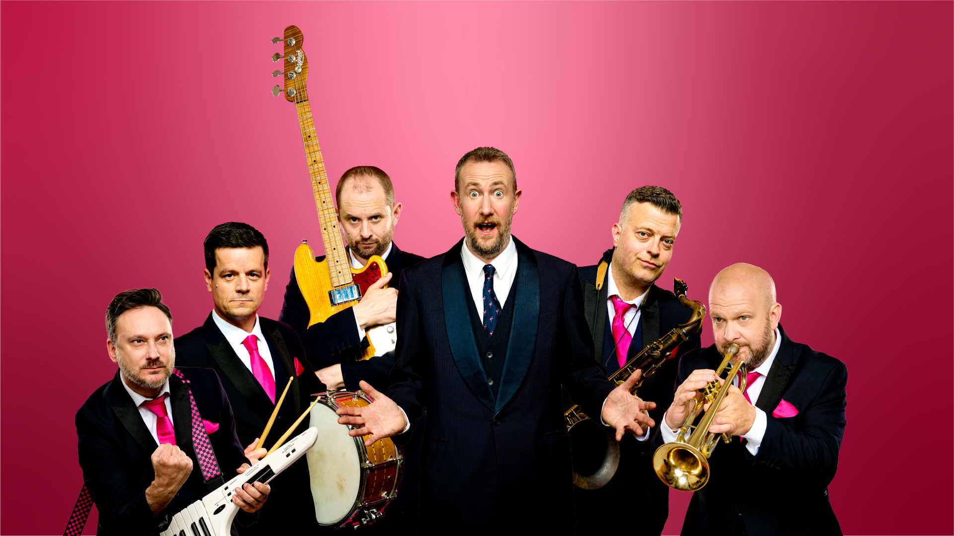 A group of six men stand in front of a pink background holding various musical instruments
